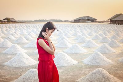 A beautiful woman in a long red dress stands tall among salt fields and blue skies.