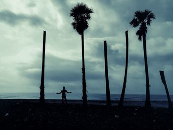 Silhouette man standing on palm tree by sea against sky
