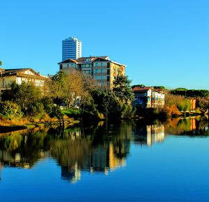 Reflection of trees and buildings in lake against clear blue sky