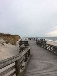 View of wooden footbridge leading towards sea against sky