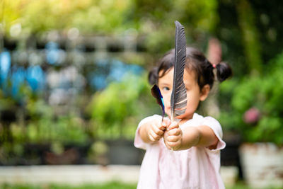 Cute little girl playing with bird feather outdoor.