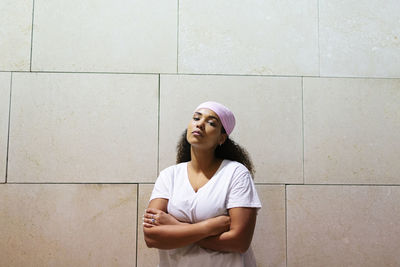 Young woman with arms crossed against wall