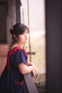 Woman looking away while standing against window