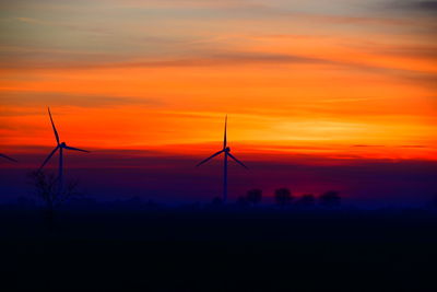 Silhouette of wind turbine against orange sky