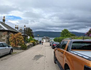 Road by buildings in city against sky