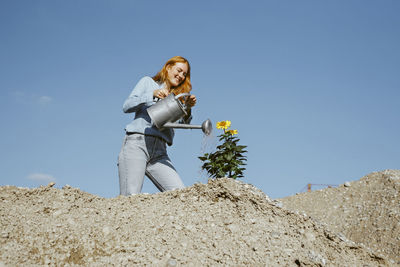 Smiling woman watering plant at construction site on sunny day