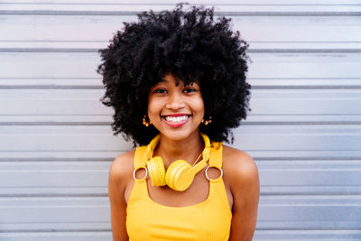 Portrait of young woman with curly hair standing against wall