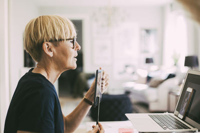 Woman working at home attending online meeting pointing at telephone display