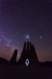 Silhouette man on rock against sky at night