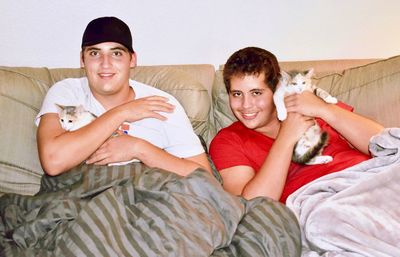 Portrait of smiling friends with cats on sofa at home