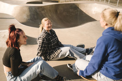 Teenage girls with skateboards sitting in skatepark