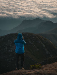 Rear view of man standing on mountain against sky