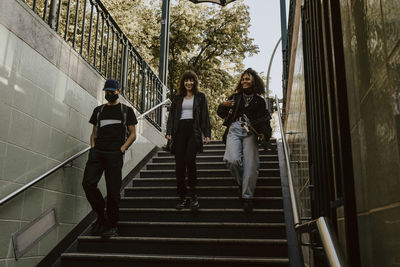 Smiling friends moving down on staircase at subway during pandemic