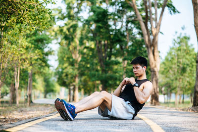 Side view of young man sitting on plant against trees