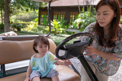 Woman standing by daughter sitting on golf cart