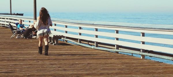 Rear view of woman walking at pier on sunny day