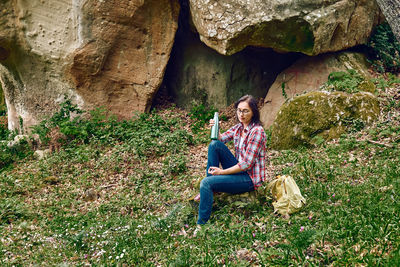 Woman sitting in forest on stone to rest, traveling with backpack in a grove or exercising outdoors