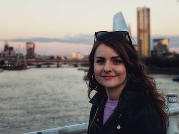 Portrait of smiling woman in city against sky during sunset