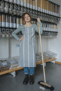 Confident store owner in apron standing with broom in zero waste shop