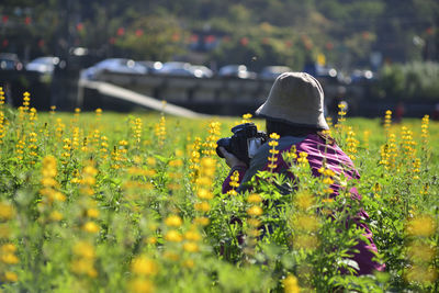 Side view of woman photographing while crouching amidst plants