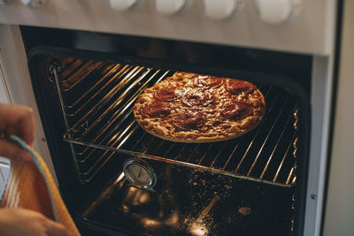 High angle view of cropped hand with napkin by pizza baking in oven at home