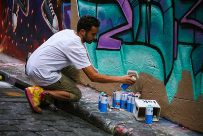 Side view of young man standing against graffiti wall