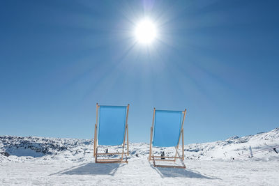 Empty lounge chairs on snow covered land against sky