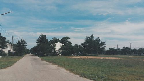 Road passing through field against cloudy sky