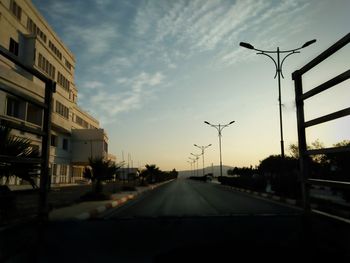 Road by city against sky during sunset