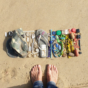 Low section of person standing barefoot next to trash and plastics collected from the beach