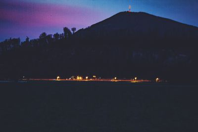 Illuminated trees by silhouette mountain against sky at night