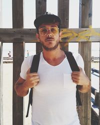 Portrait of young man wearing sunglasses against fence