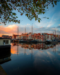 Sailboats moored at harbor against sky during sunset