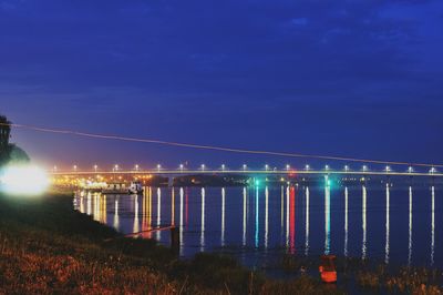 Illuminated bridge over sea against sky at night