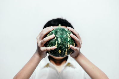 Boy covering face with watermelon against white background