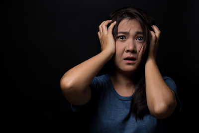 Portrait of scared young woman standing against black background