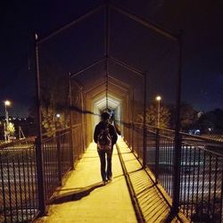 Rear view of men walking on illuminated bridge at night