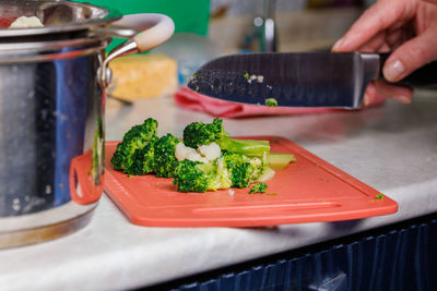 Close-up view of elder white woman hands slicing green broccoli with kitchen knife