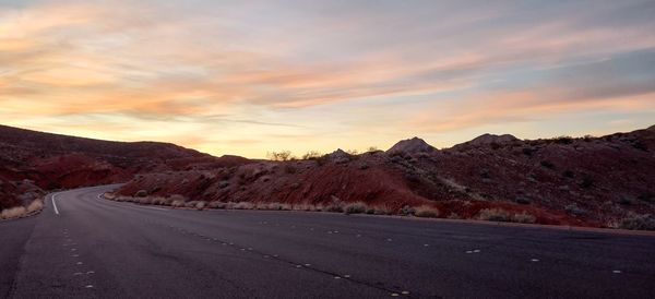 Road by mountains against sky during sunset