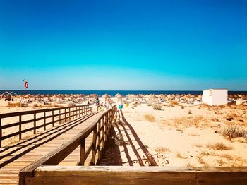 Wooden pier at beach against clear blue sky during sunny day