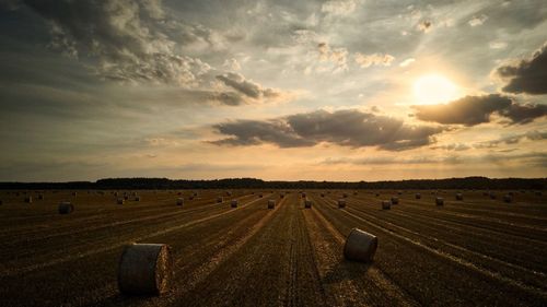 Hay bales on field against sky during sunset