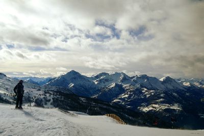 Rear view of young man skiing on snowcapped mountain against cloudy sky