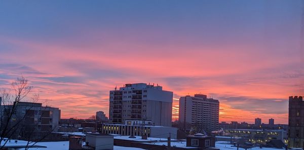 Buildings in city against romantic sky at sunset