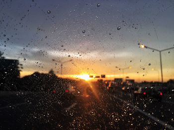 Raindrops on glass window against sky during sunset