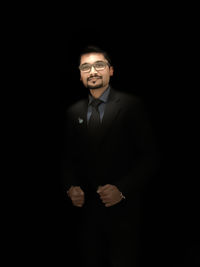 Portrait of young man standing against black background