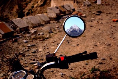 Reflection of mountain on motorcycle mirror during sunny day