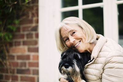 Portrait of happy senior woman with dog outside house