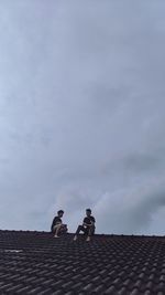 Low angle view of men on roof against sky