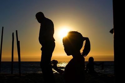 Side view of silhouette girl and man on pier by sea during sunset