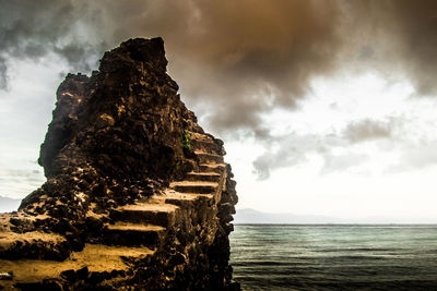 Rock formation by sea against sky